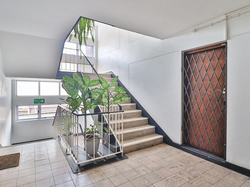 Communal apartment hallway featuring a staircase with metal balustrades, tiled flooring, and a secure entrance door with a metal security gate.