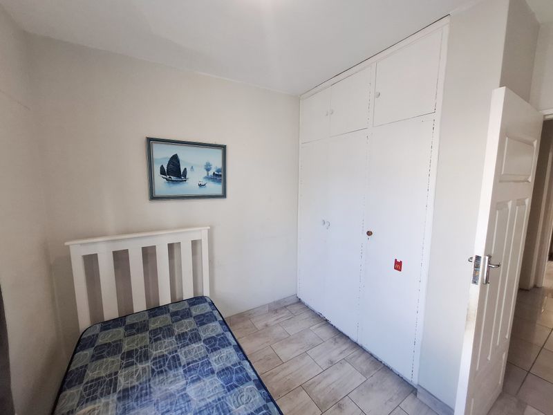 A bedroom featuring tiled flooring and built-in cupboards with some visible wear on the cabinetry finish.