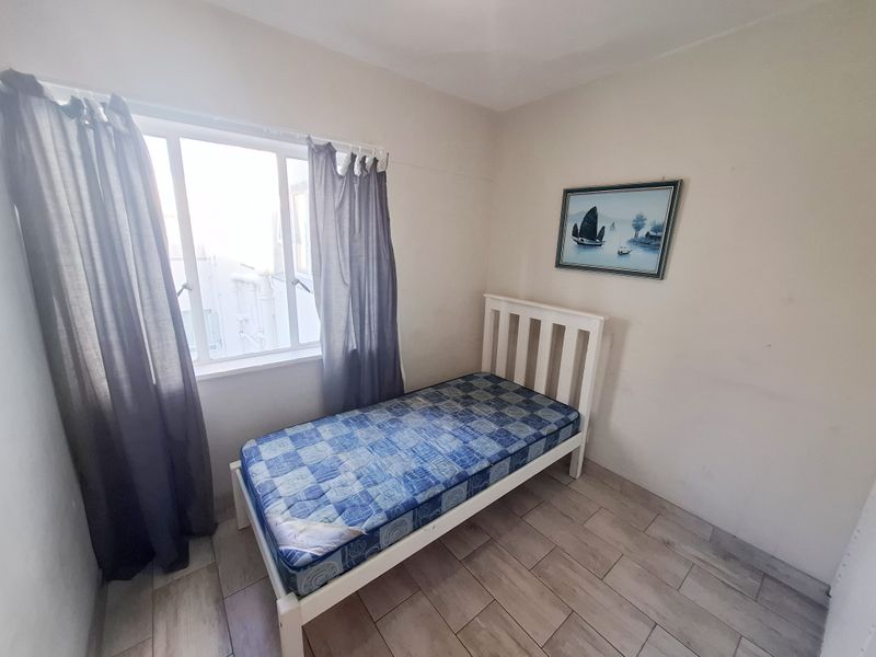 A compact bedroom featuring tiled flooring and a window, providing a functional space for a single bed.