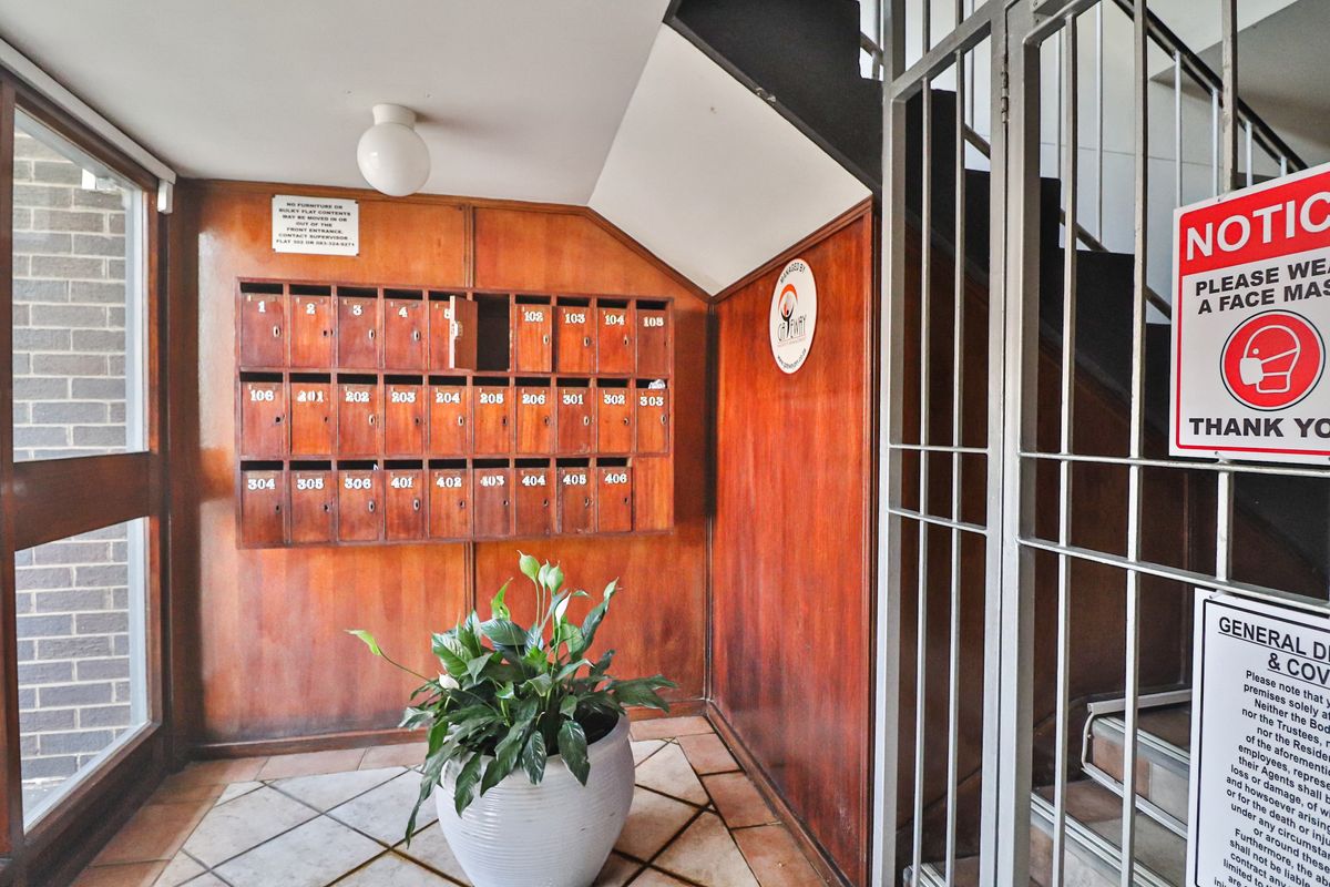 Apartment building entrance foyer featuring wooden mailboxes, tiled flooring, and a secure metal gate.
