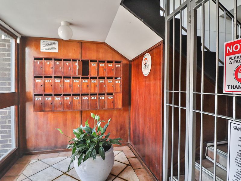 Apartment building entrance foyer featuring wooden mailboxes, tiled flooring, and a secure metal gate.