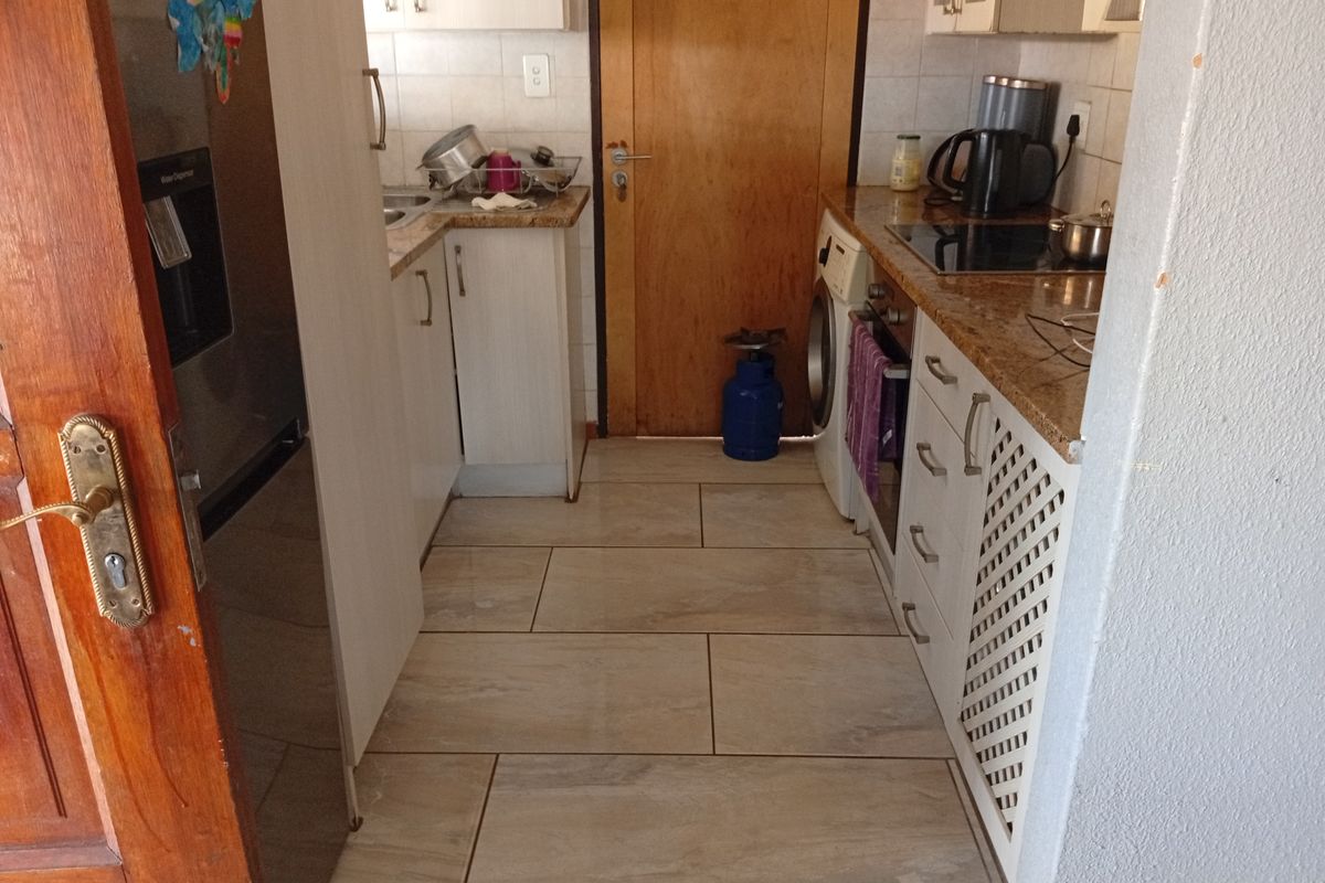 Compact kitchen featuring granite countertops, built-in oven, hob, and tiled flooring with direct access to an adjacent room.