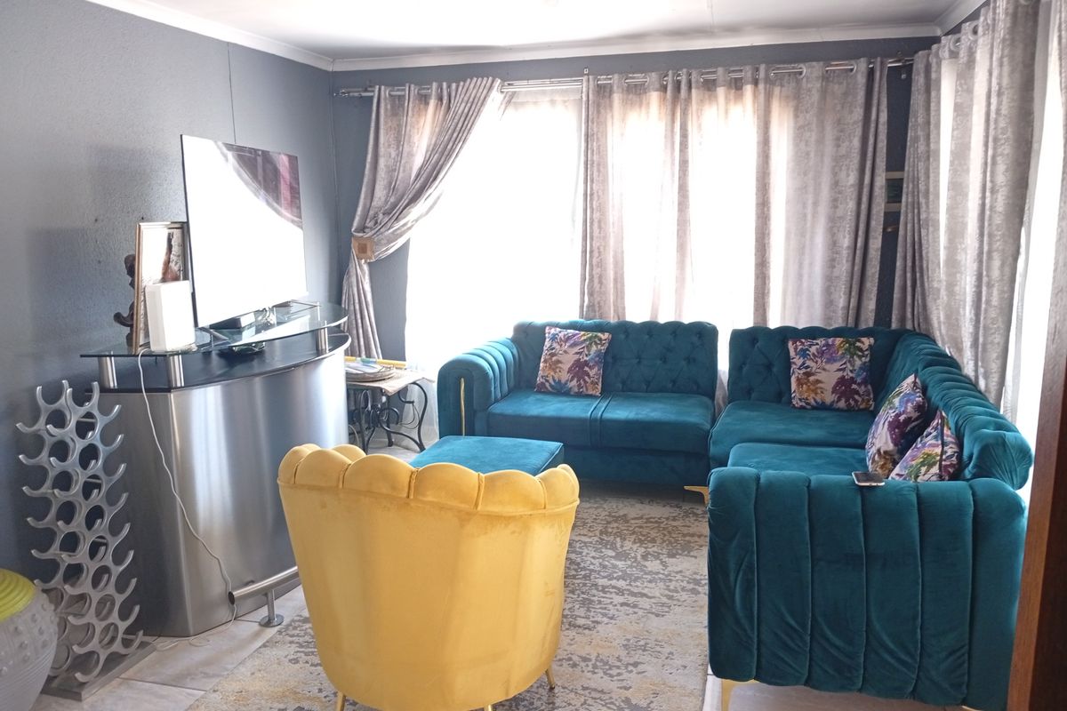 A comfortable living room featuring tiled flooring and large windows with curtains, providing a bright and inviting space for relaxation.