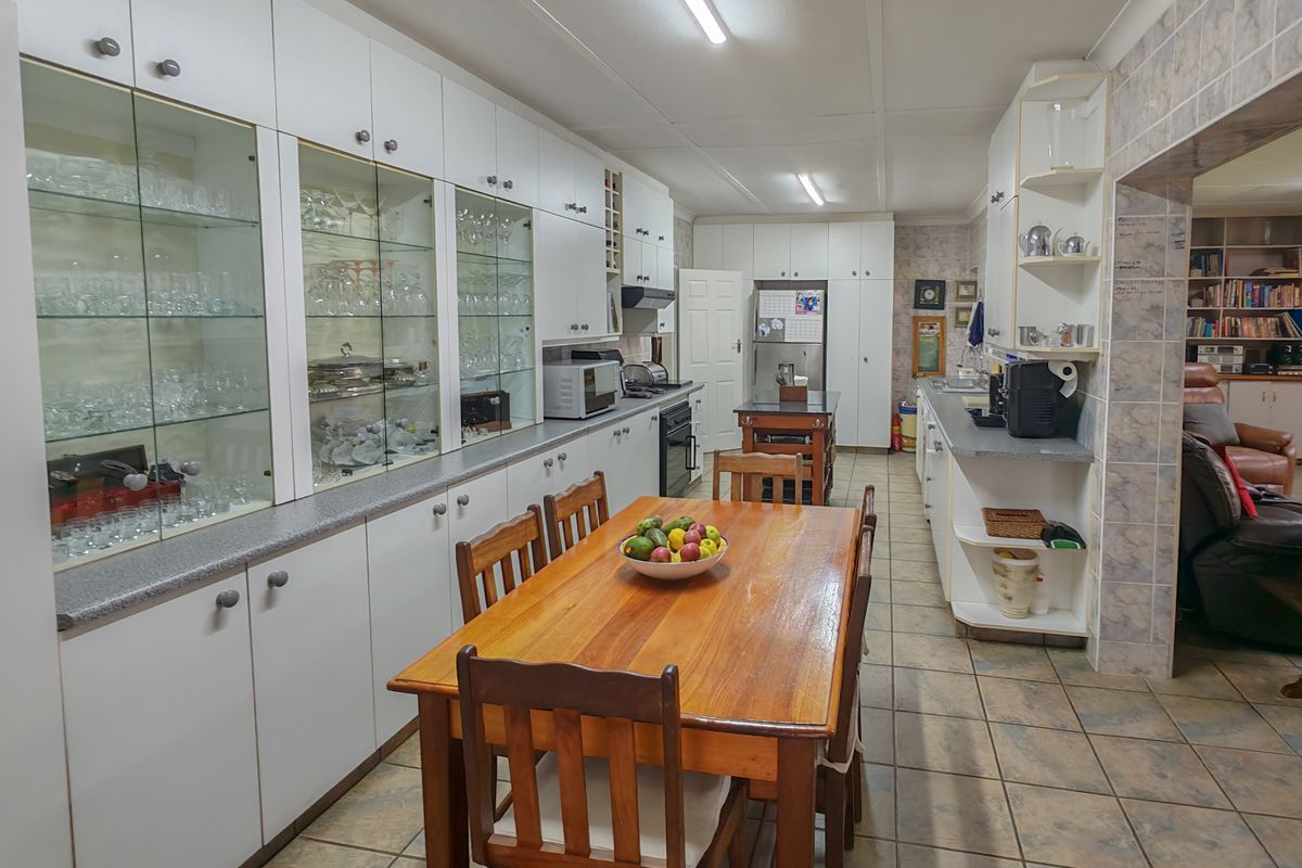 Spacious kitchen featuring extensive white cabinetry, built-in oven and hob, tiled flooring, and a dedicated dining area with ample storage space.