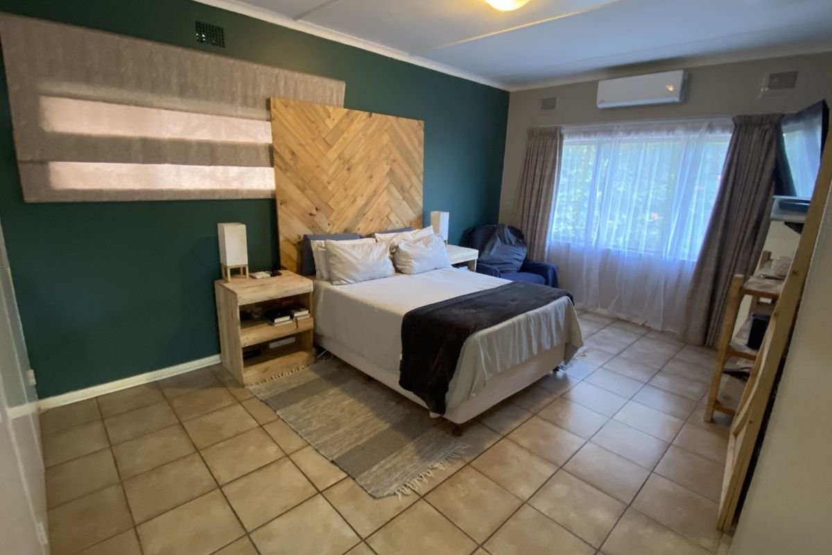 A bedroom featuring tiled flooring, a wall-mounted air conditioning unit, and a decorative wooden headboard feature wall.
