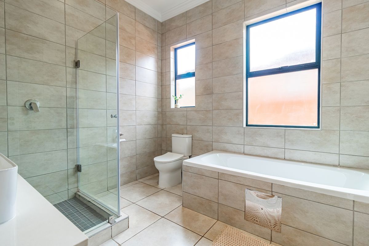 A modern bathroom featuring a glass-enclosed shower, a built-in bathtub with tiled surround, and a toilet, finished with neutral floor-to-ceiling wall tiles.