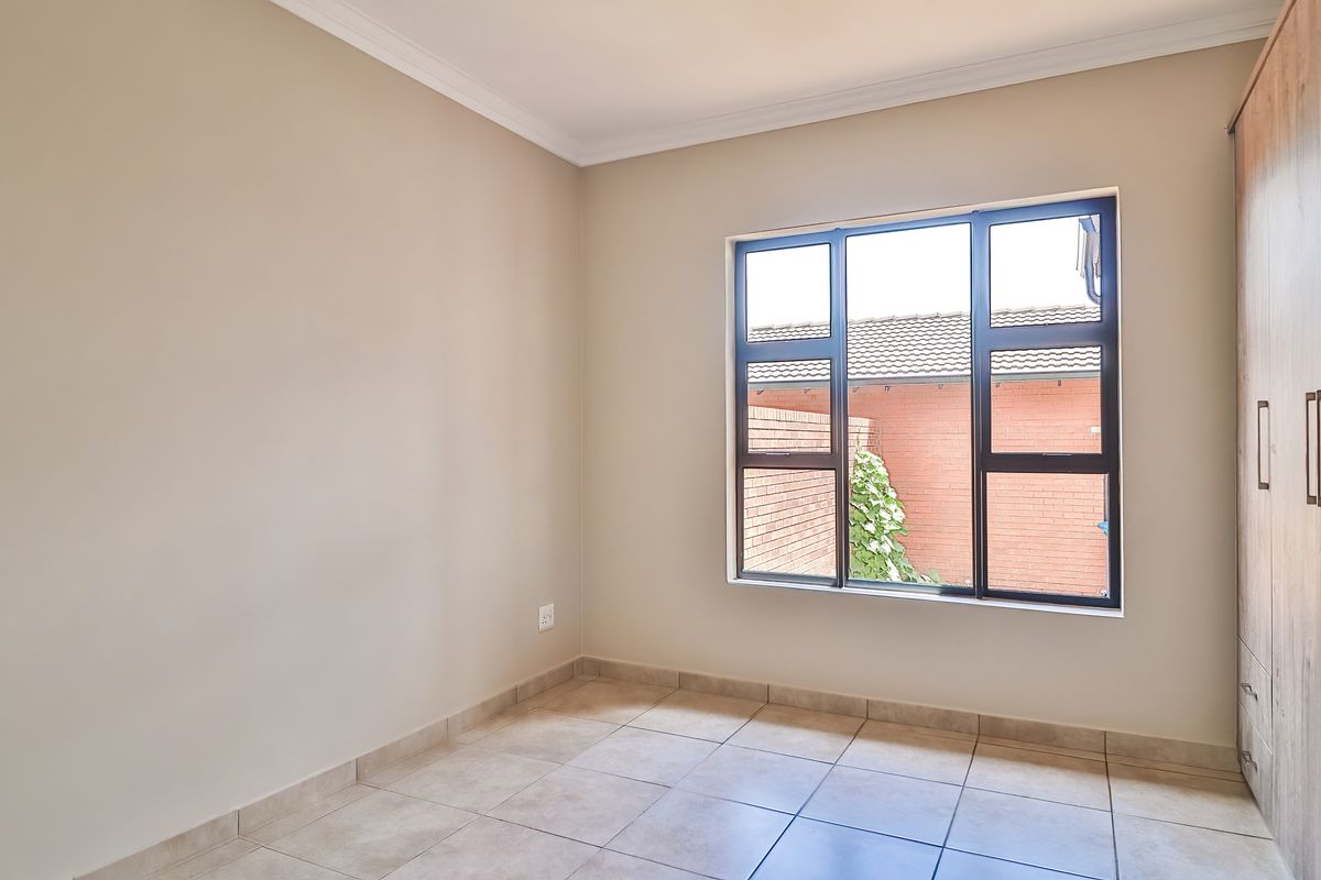A bright, empty bedroom featuring neutral tiled flooring, built-in wooden cabinetry, and a large window overlooking the rear exterior.