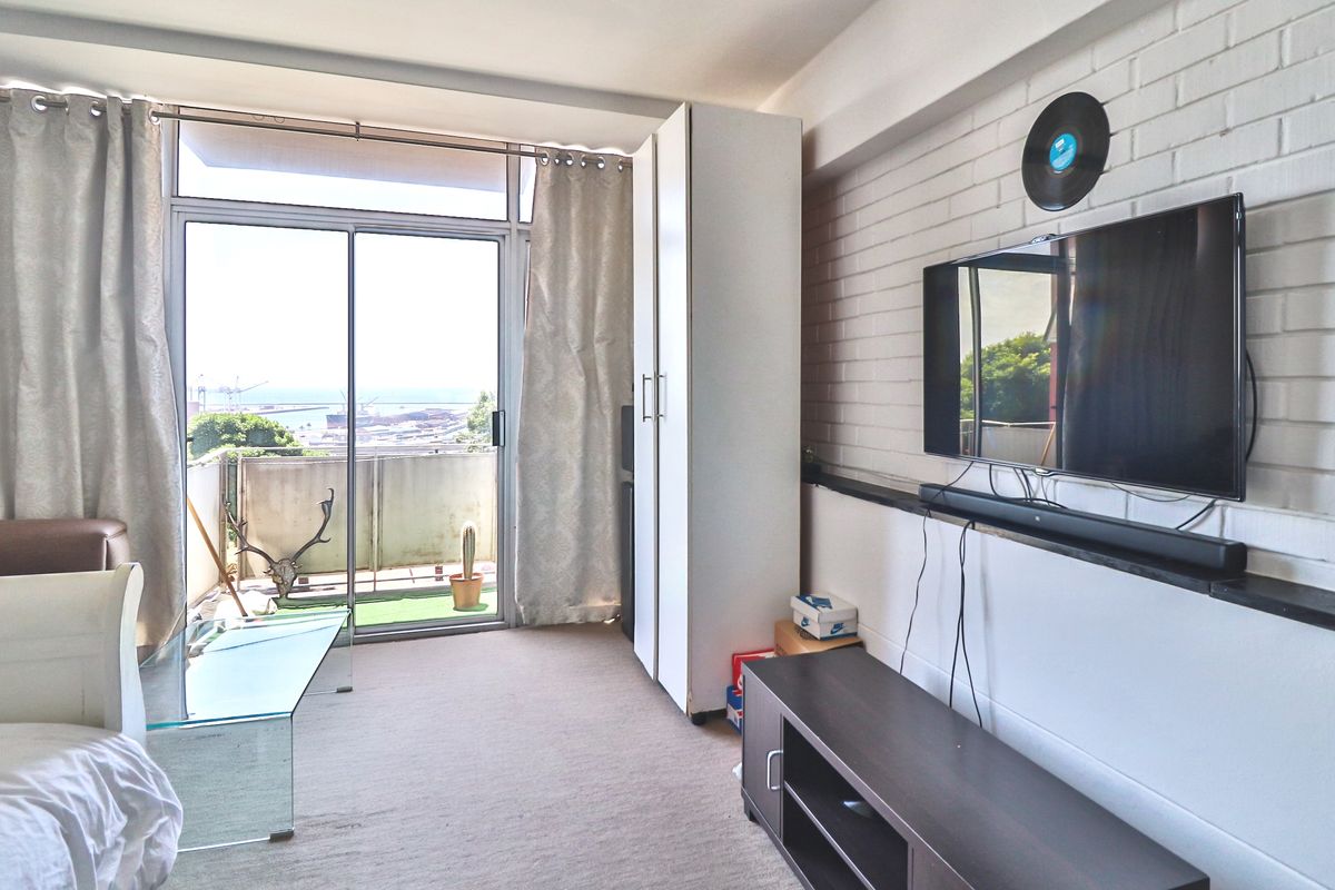 Living area featuring a painted brick feature wall, built-in storage cupboard, and sliding glass doors leading to a balcony with coastal views.