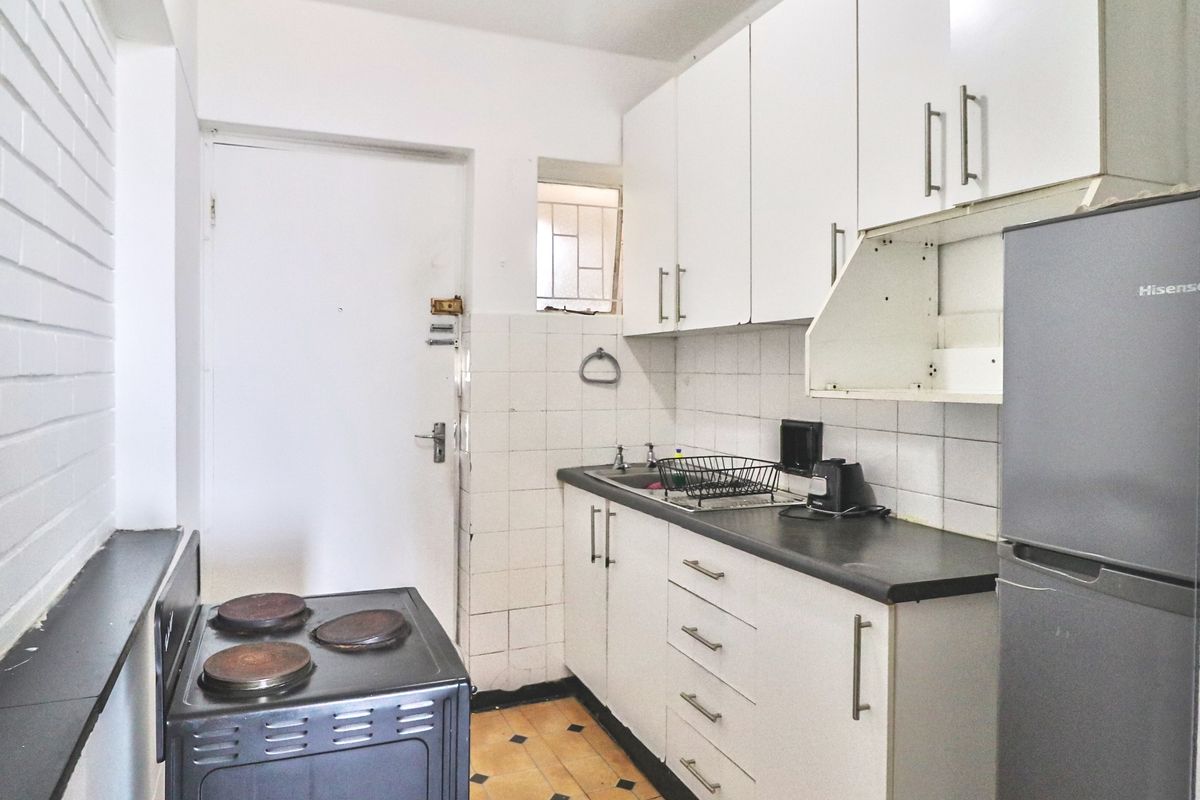 A compact kitchen featuring white cabinetry, a dark countertop, a freestanding stove, and tiled flooring, offering a functional layout with potential for modernization.