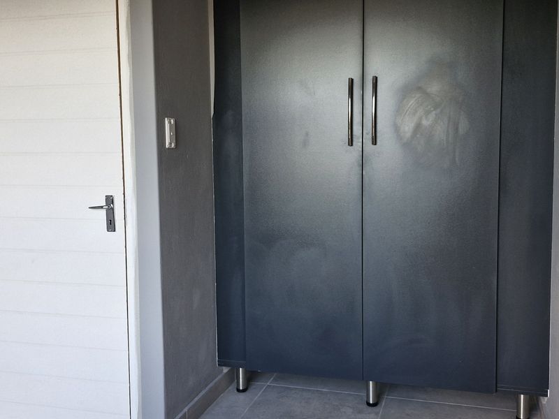 A functional hallway space featuring a built-in dark grey cupboard and tiled flooring, providing practical storage within the apartment.