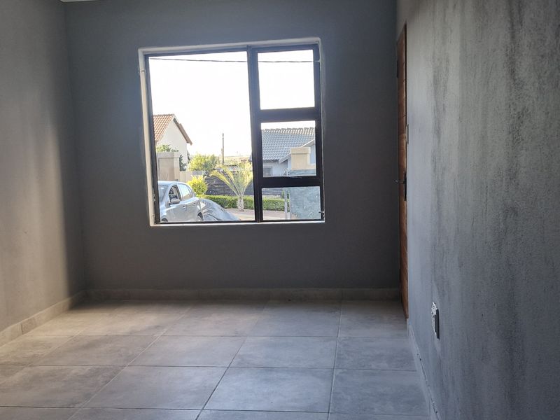 An empty living room featuring grey tiled flooring and an aluminium window, currently requiring final wall finishing and painting.