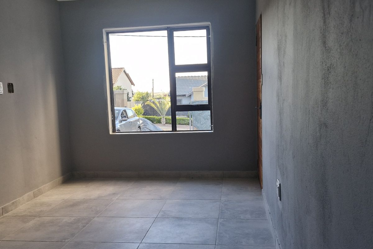 An empty living room featuring grey tiled flooring and an aluminium window, currently requiring final wall finishing and painting.