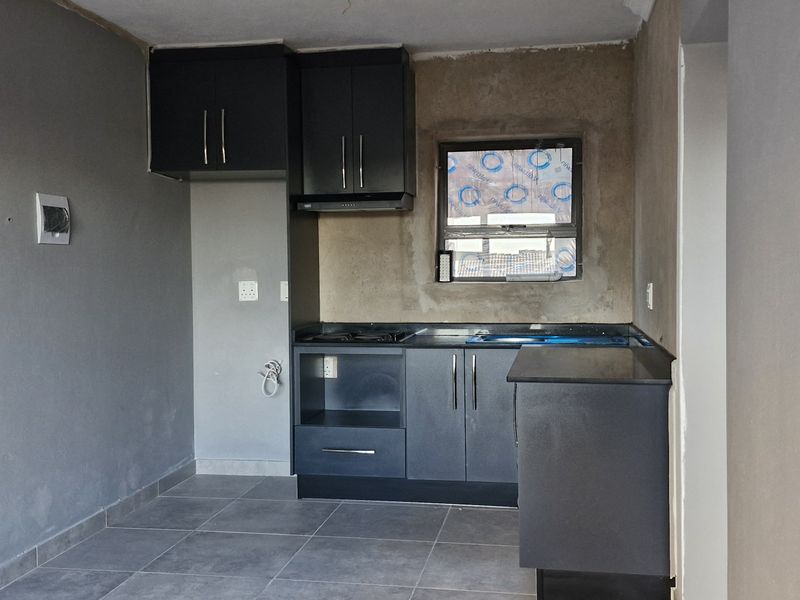 A compact kitchen area featuring dark cabinetry, a built-in hob, and extractor fan, currently requiring final wall finishing and plastering.
