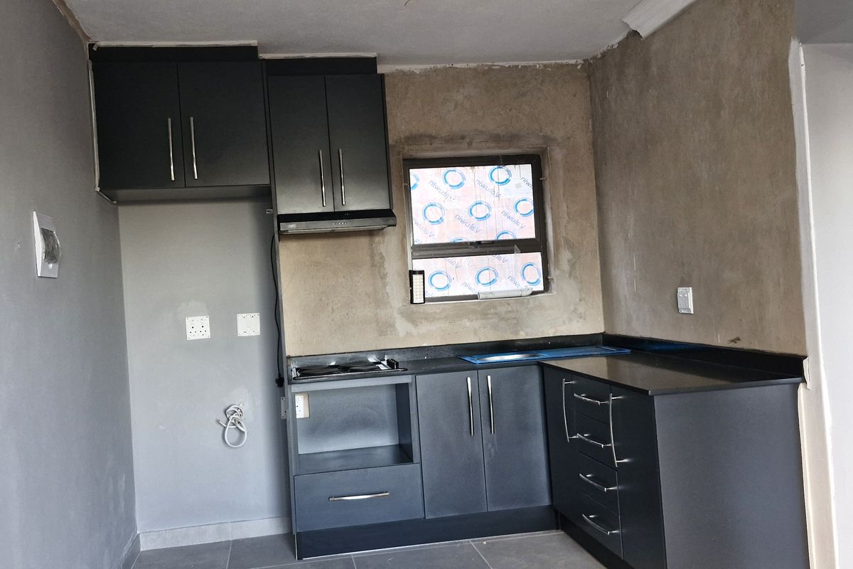 A compact kitchen featuring dark cabinetry, black stone countertops, and a built-in hob, currently requiring final wall finishes and minor electrical completion.