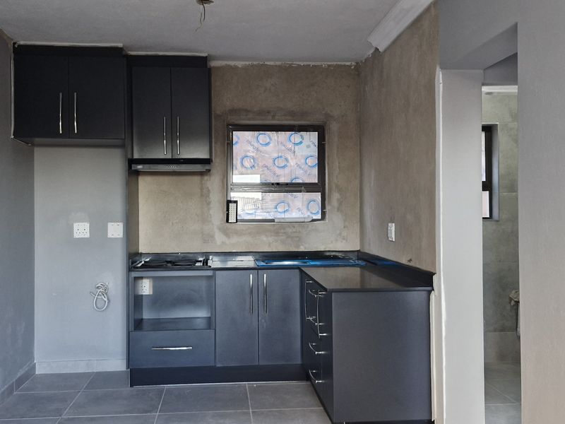 A compact kitchen featuring dark cabinetry and a built-in hob, currently requiring finishing touches to the walls and backsplash to complete the space.