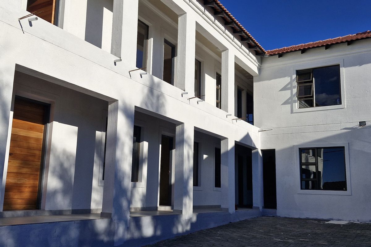 A well-maintained rear exterior view of the apartment building featuring a covered patio, paved courtyard, and modern aluminium window frames.