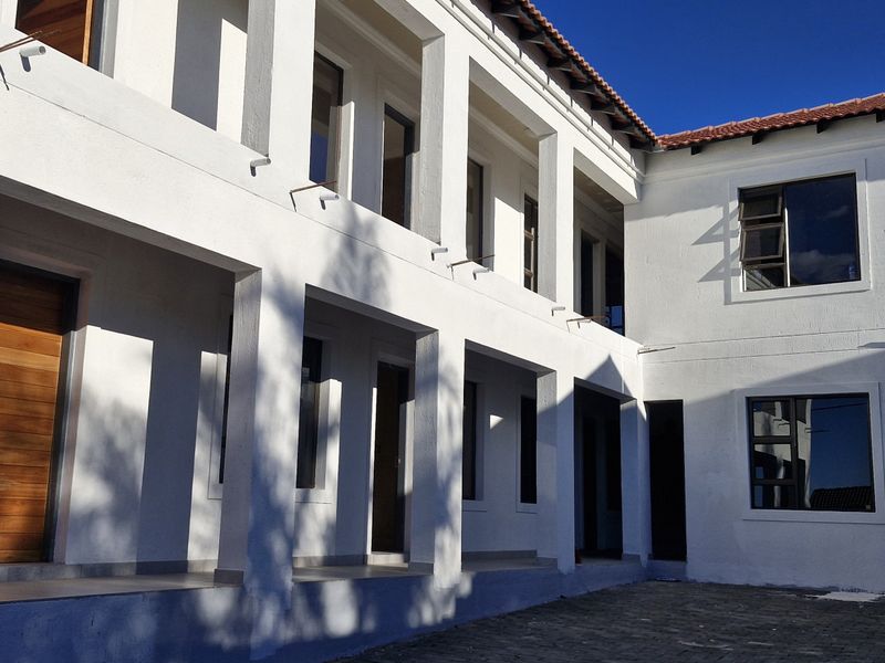 A well-maintained rear exterior view of the apartment building featuring a covered patio, paved courtyard, and modern aluminium window frames.