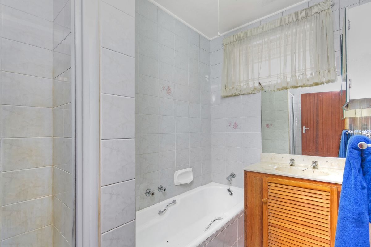 A functional bathroom featuring a built-in bathtub, tiled walls, and a wooden vanity cabinet with an integrated sink.