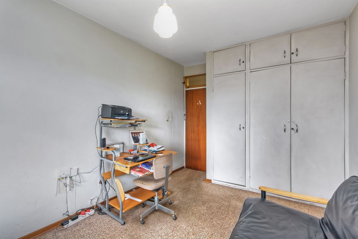 A bedroom featuring built-in storage cupboards, carpeted flooring, and a wooden door, offering a functional space with potential for cosmetic updates.