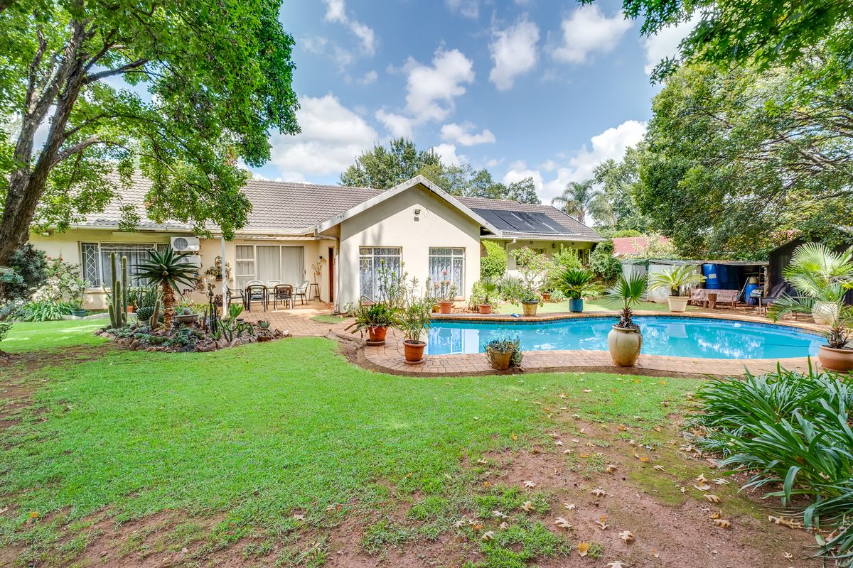 A spacious rear garden featuring a swimming pool with brick coping, a paved patio area, and established landscaping.