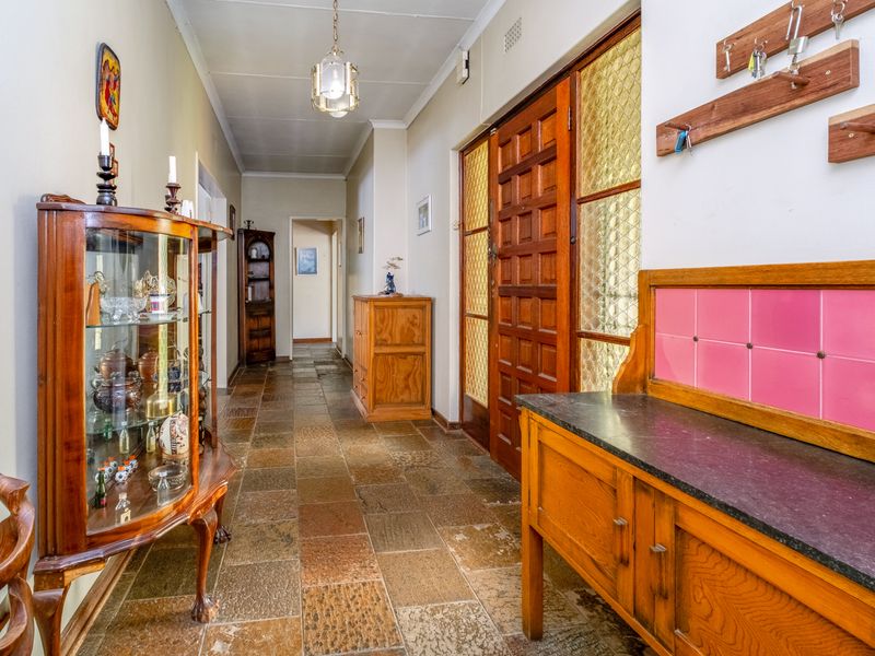 A spacious hallway featuring durable stone tile flooring, a classic timber-framed glass door, and a built-in wooden console with a stone countertop.