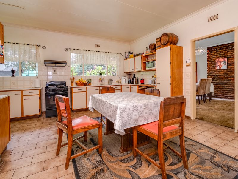 A functional kitchen featuring built-in cabinetry, a freestanding stove with extractor fan, and tiled flooring, with an adjacent dining area visible through the doorway.