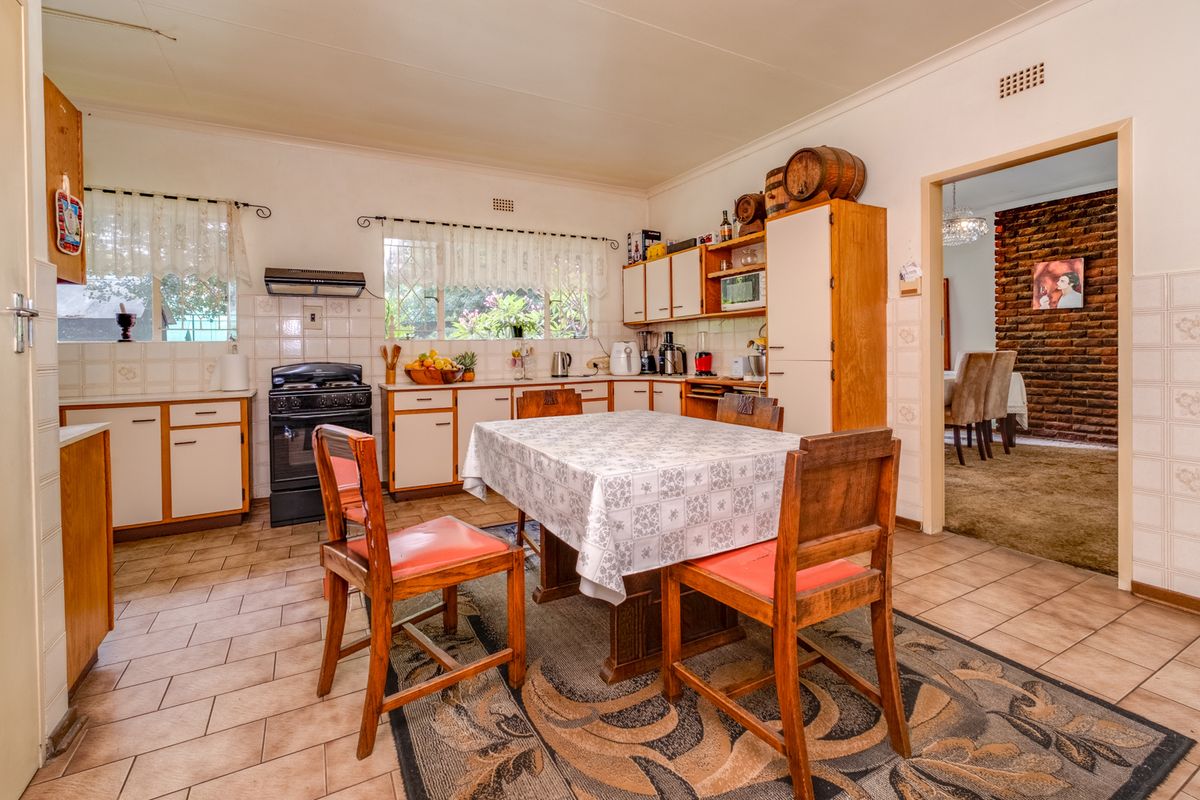 A functional kitchen featuring built-in cabinetry, a freestanding stove with extractor fan, and tiled flooring, with an adjacent dining area visible through the doorway.