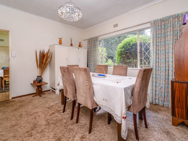 A dining room featuring a large window with garden views, neutral walls, and a central chandelier, providing a functional space for family meals.