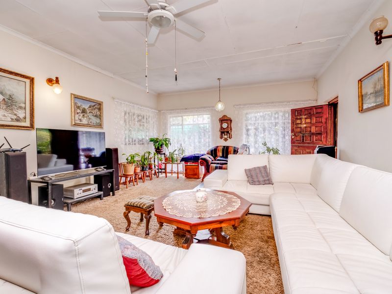 A spacious living room featuring a ceiling fan, wall-mounted lighting, and large windows, providing a comfortable and functional area for relaxation.