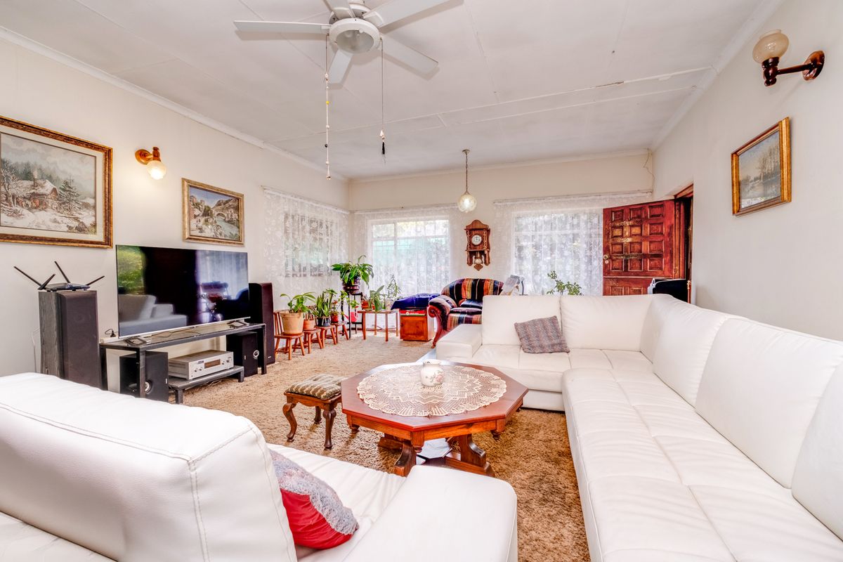 A spacious living room featuring a ceiling fan, wall-mounted lighting, and large windows, providing a comfortable and functional area for relaxation.