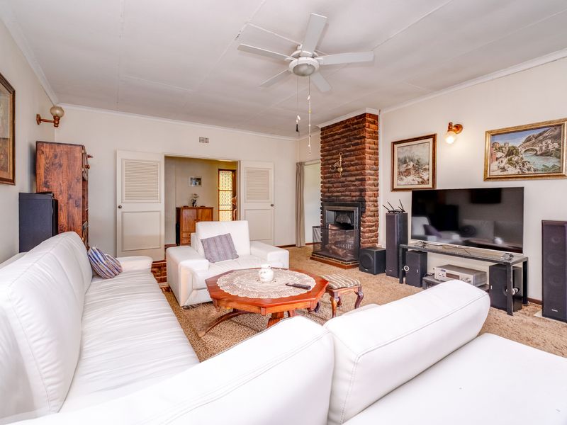 A cozy living room featuring a prominent brick fireplace, ceiling fan, and double door access to adjacent rooms.
