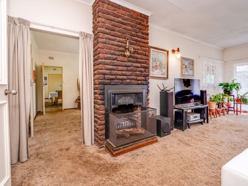 A living room featuring a prominent brick fireplace, carpeted flooring, and an open transition to an adjacent room.