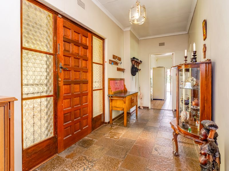 A traditional entrance hallway featuring a solid timber front door with decorative glass panels and durable stone-style floor tiling.