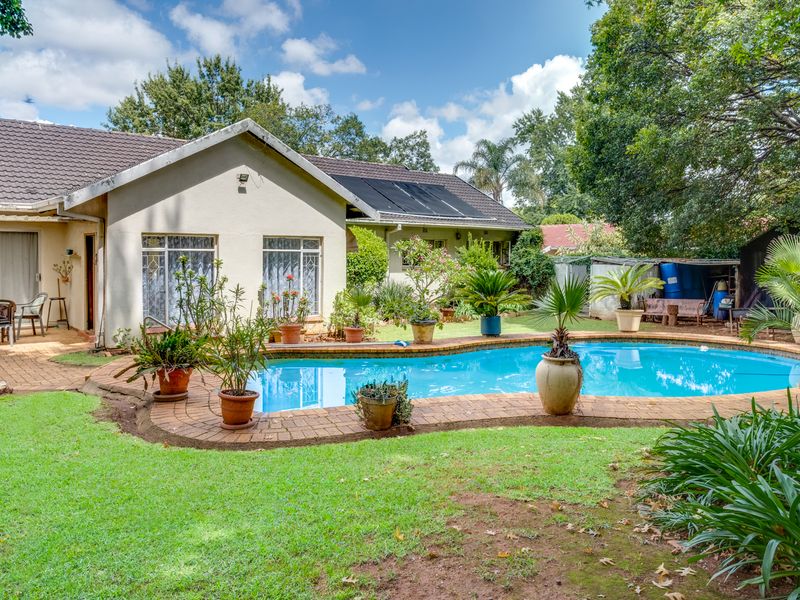 A spacious rear garden featuring a swimming pool with brick surround, paved patio area, and established landscaping, ideal for outdoor relaxation and entertainment.