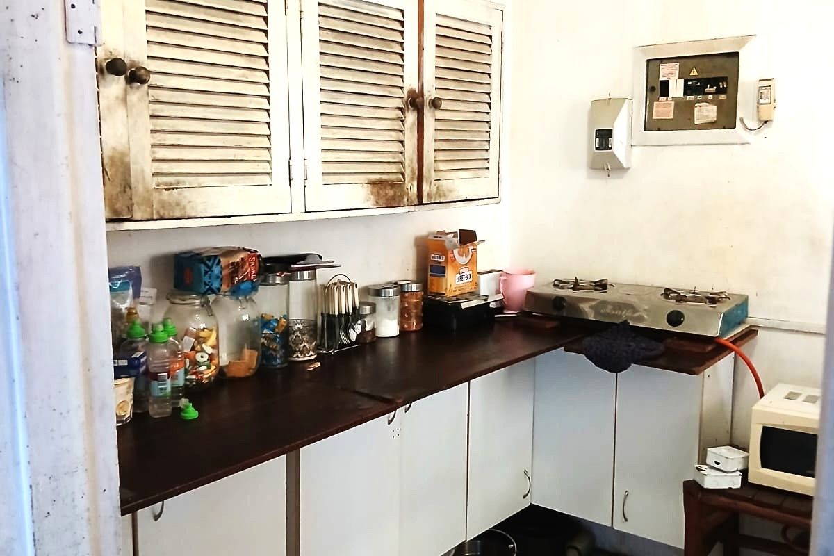 A compact kitchen area featuring dated louvered cabinetry, dark laminate countertops, and a built-in electrical distribution board.