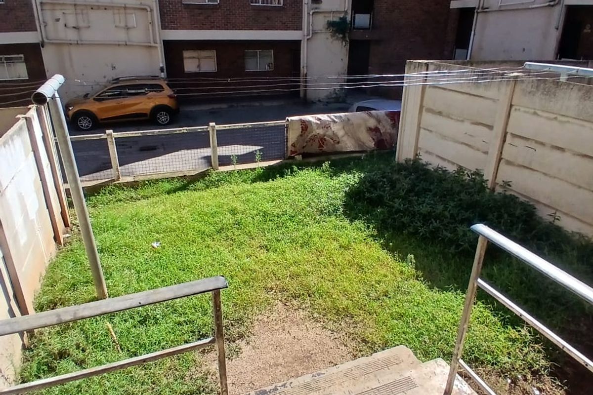 A small, private rear garden area featuring concrete steps with metal railings, leading to a grassed yard enclosed by boundary walls.