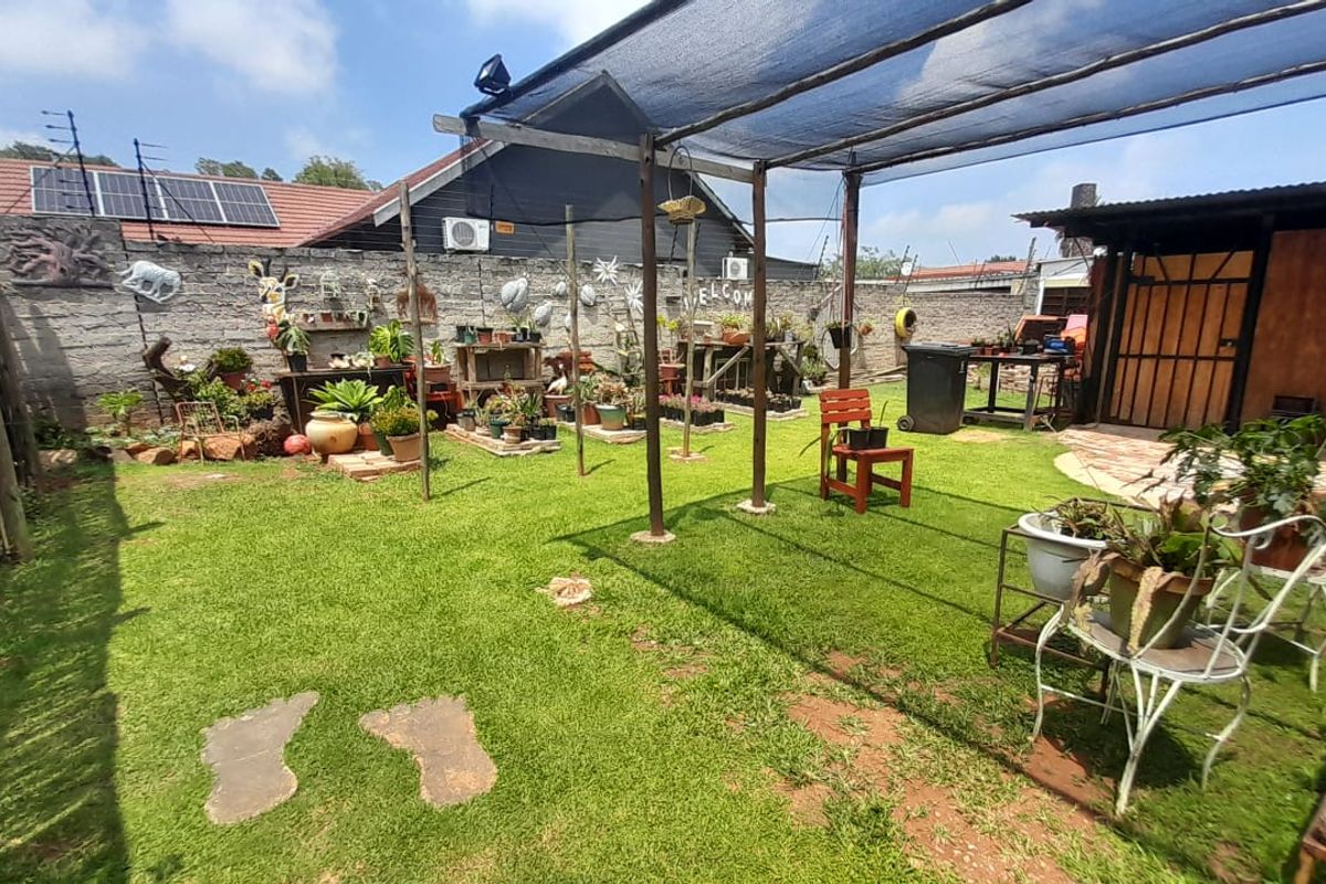 A private rear garden featuring a lawn area, a shaded patio structure, and perimeter walling with integrated solar panels visible on the main roof.