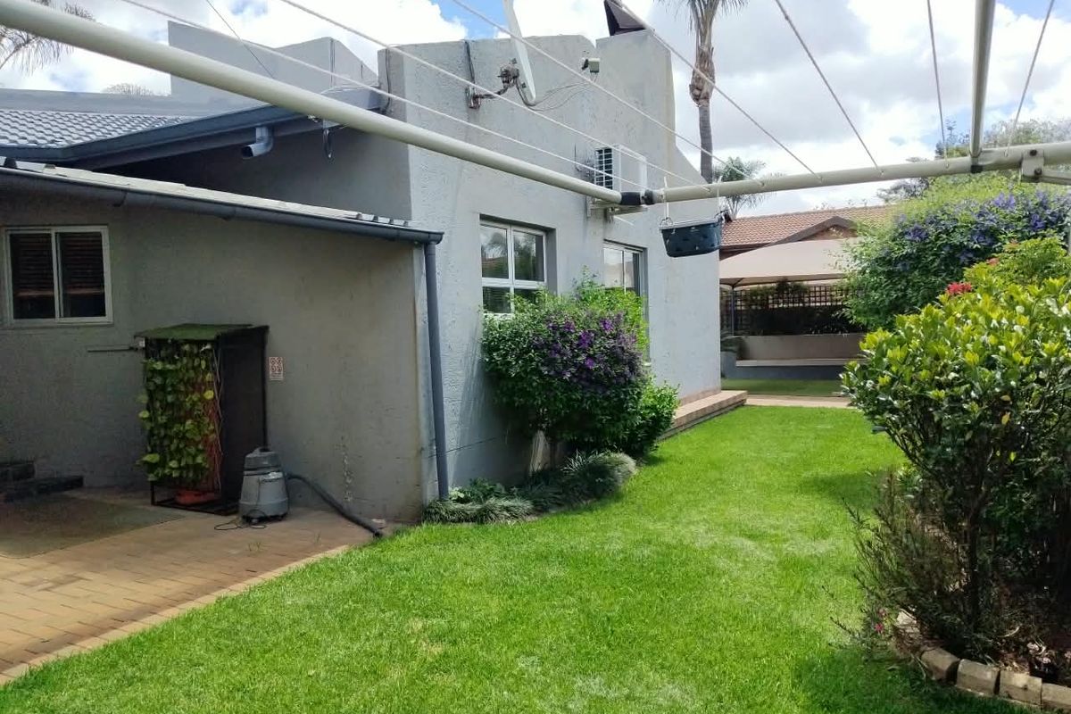Rear exterior view of the house featuring a paved patio area, a well-maintained lawn, and fixed utility installations including an air conditioning unit.