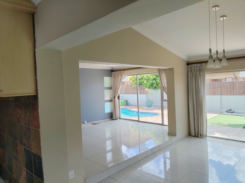 Spacious open-plan living area featuring polished tiled floors, vaulted ceilings, and large sliding glass doors providing seamless access to the outdoor pool area.