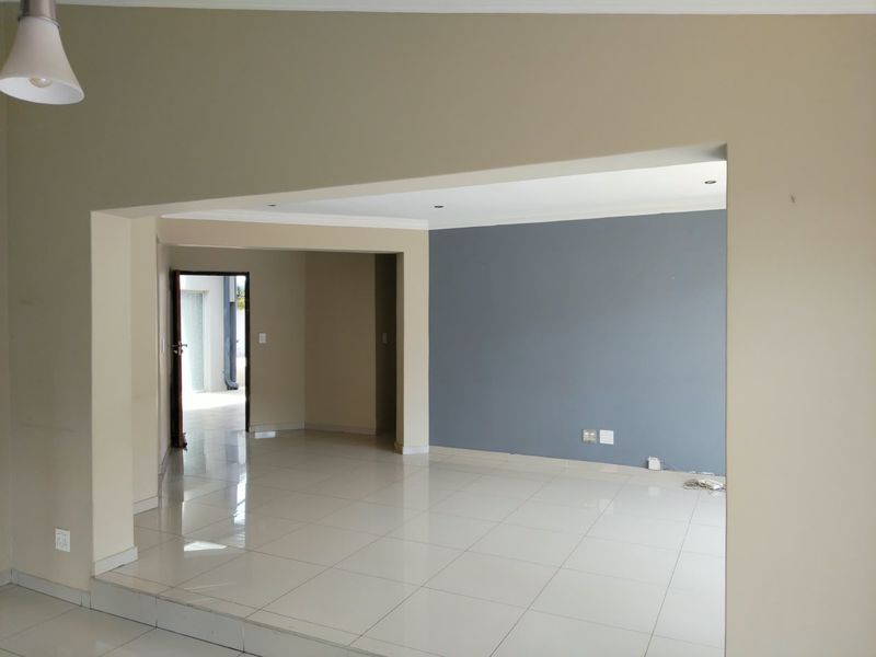 An empty, open-plan living area featuring neutral and accent-colored walls, tiled flooring, and recessed lighting, offering a clean and versatile space.