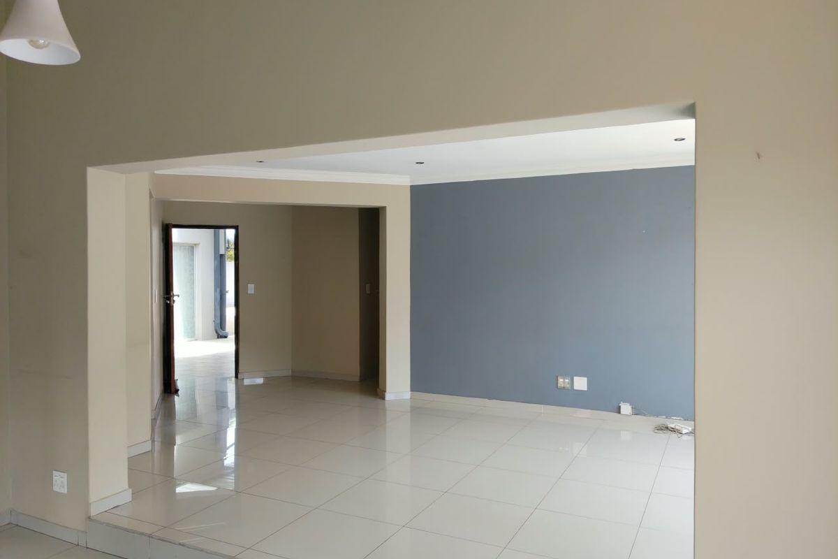 An empty, open-plan living area featuring neutral and accent-colored walls, tiled flooring, and recessed lighting, offering a clean and versatile space.
