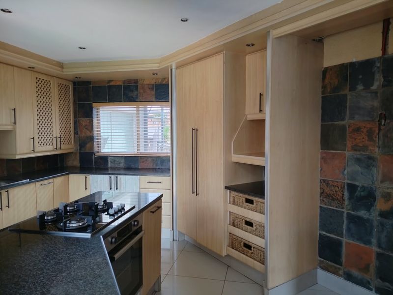 Kitchen featuring light wood cabinetry, granite countertops, a central island with a gas hob, and a distinctive slate tile backsplash.