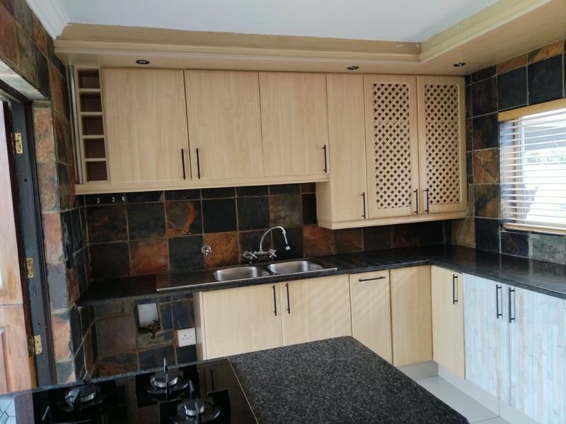 A functional kitchen featuring light wood cabinetry, granite countertops, a double sink, and a distinctive slate tile backsplash with an integrated gas hob.