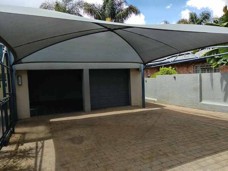 A double garage featuring a modern shade sail structure over a paved driveway area.