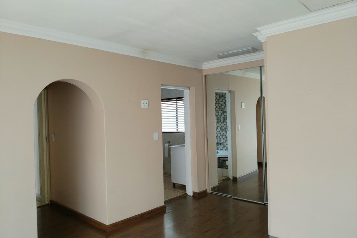 A spacious bedroom featuring laminate flooring, mirrored built-in cupboards, and an arched entryway leading to an en-suite bathroom.