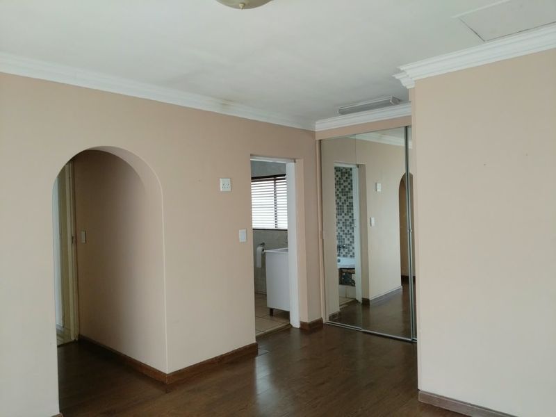 A spacious bedroom featuring laminate flooring, mirrored built-in cupboards, and an arched entryway leading to an en-suite bathroom.