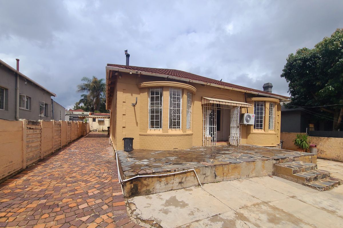 Rear view of the house featuring a stone patio, bay windows, and brick-paved driveway area with boundary walling.