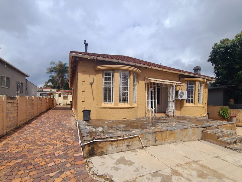 Rear view of the house featuring a stone patio, bay windows, and brick-paved driveway area with boundary walling.
