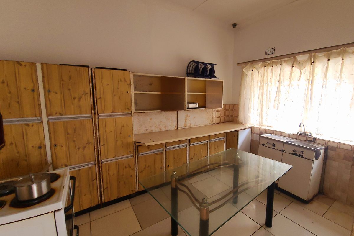 A dated kitchen featuring wooden cabinetry, laminate countertops, and tiled flooring, offering significant potential for modernization and renovation.