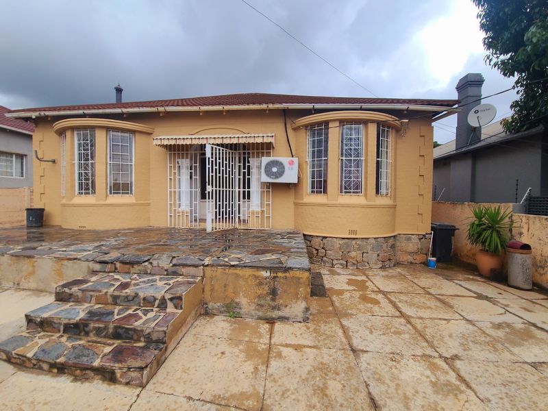 Front elevation of a house featuring a stone-clad patio, bay windows, security gates, and an exterior air conditioning unit.